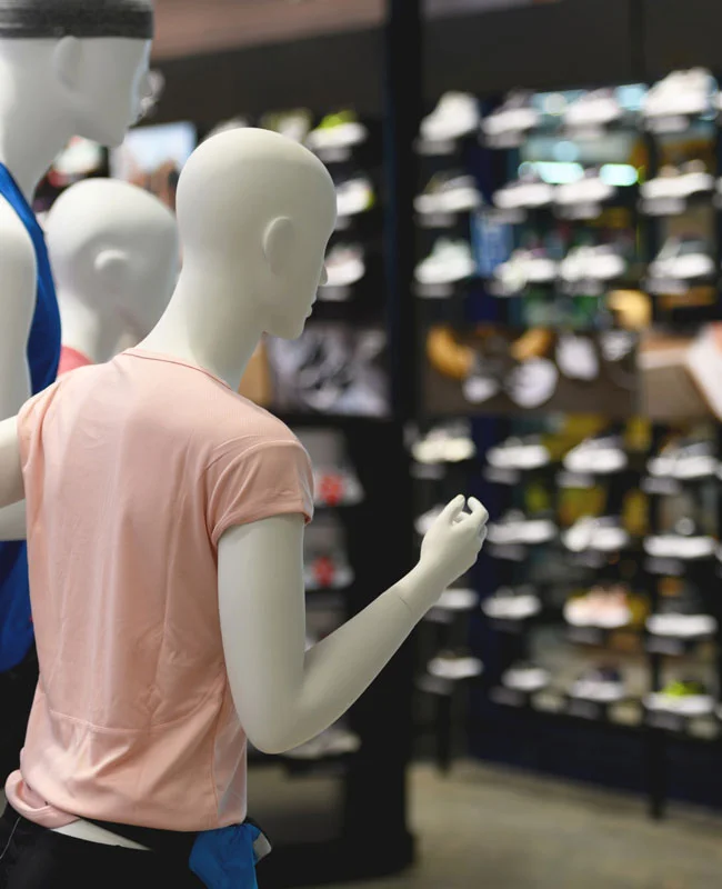 Maniquíes con ropa deportiva en el interior de una tienda de retail con estantes de calzado al fondo.