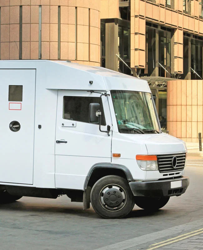 Camión blindado blanco de transporte de valores estacionado frente a un edificio financiero.